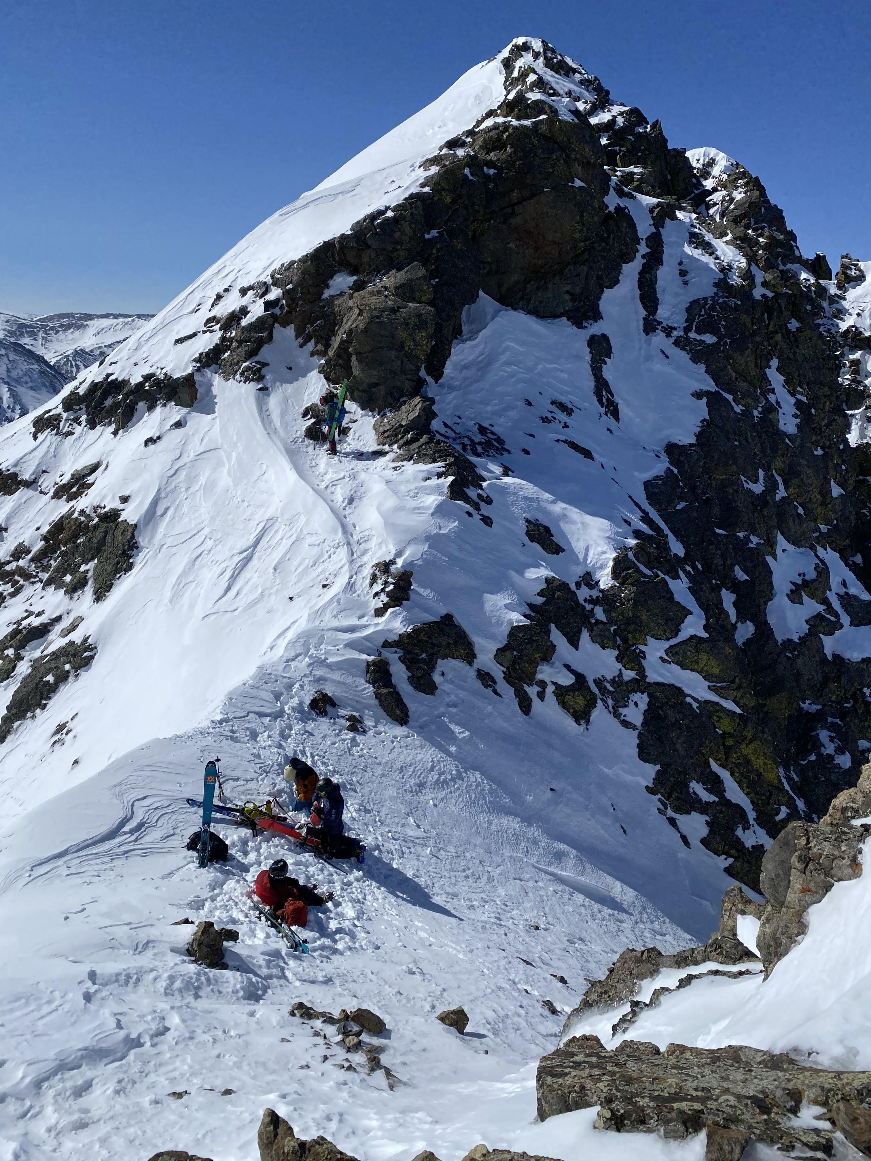 Three mountaineers sitting at the top of a couloir in snowy saddle