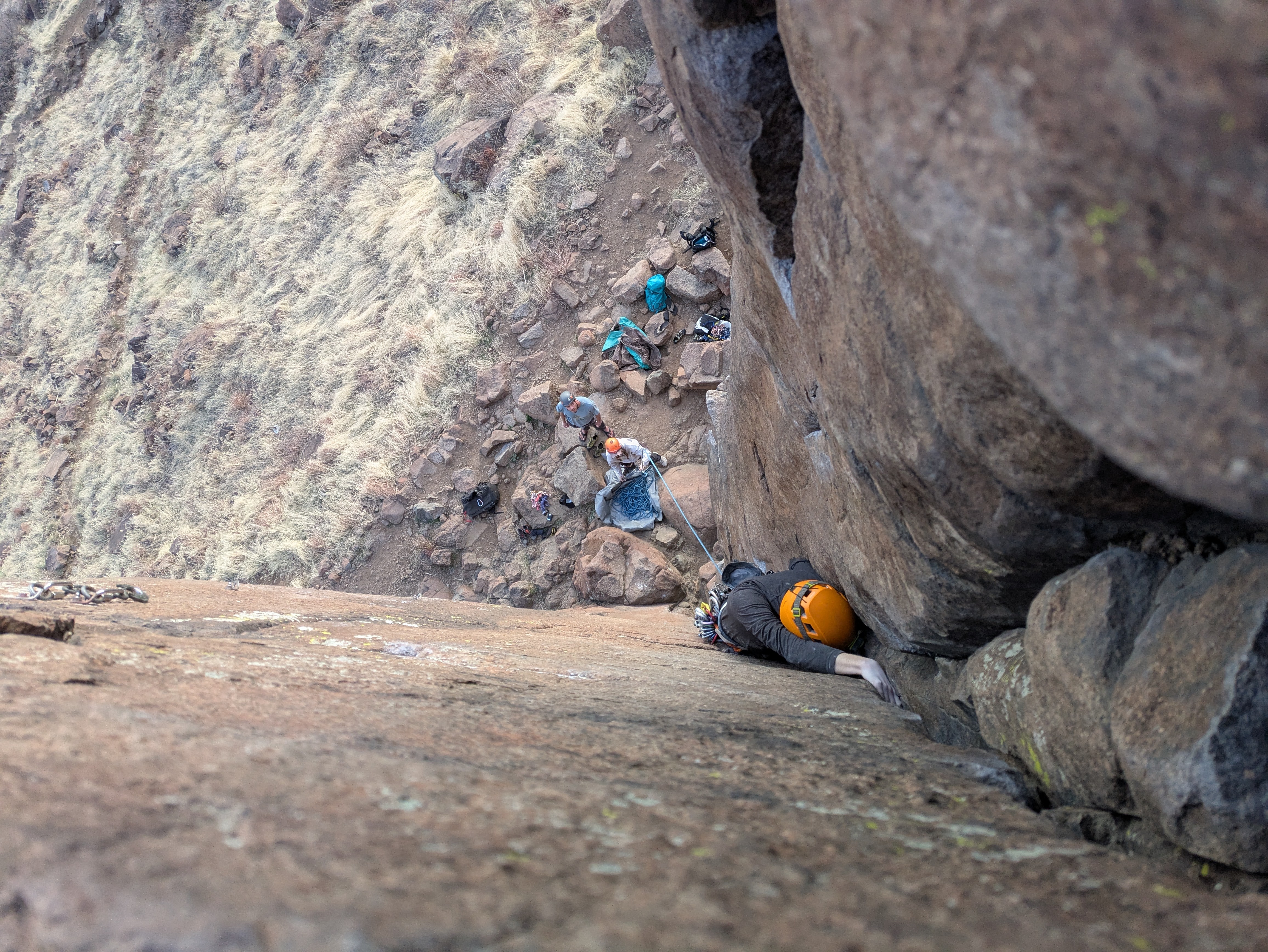 Person climbing up a crack, hand above their head with their helmet wedged in the rock